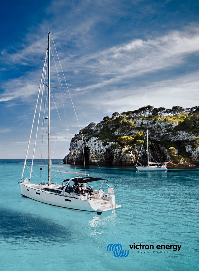 Sailboat anchored in clear turquoise water near rocky coastline, powered by Victron Energy marine solar system